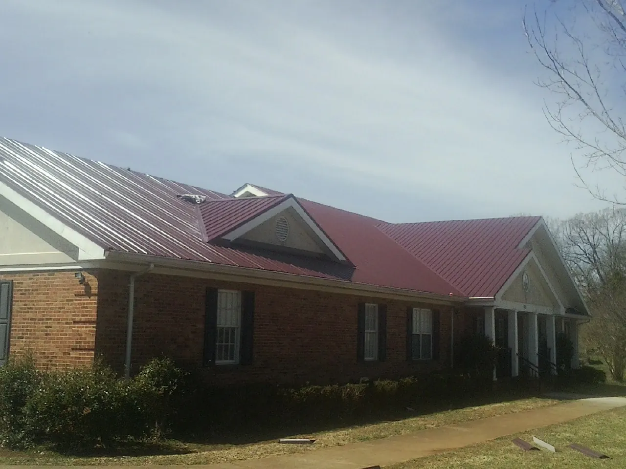 Red metal roof with gabled entries on a long brick building, from a Hail Damage Roof Repair job in Woodacre