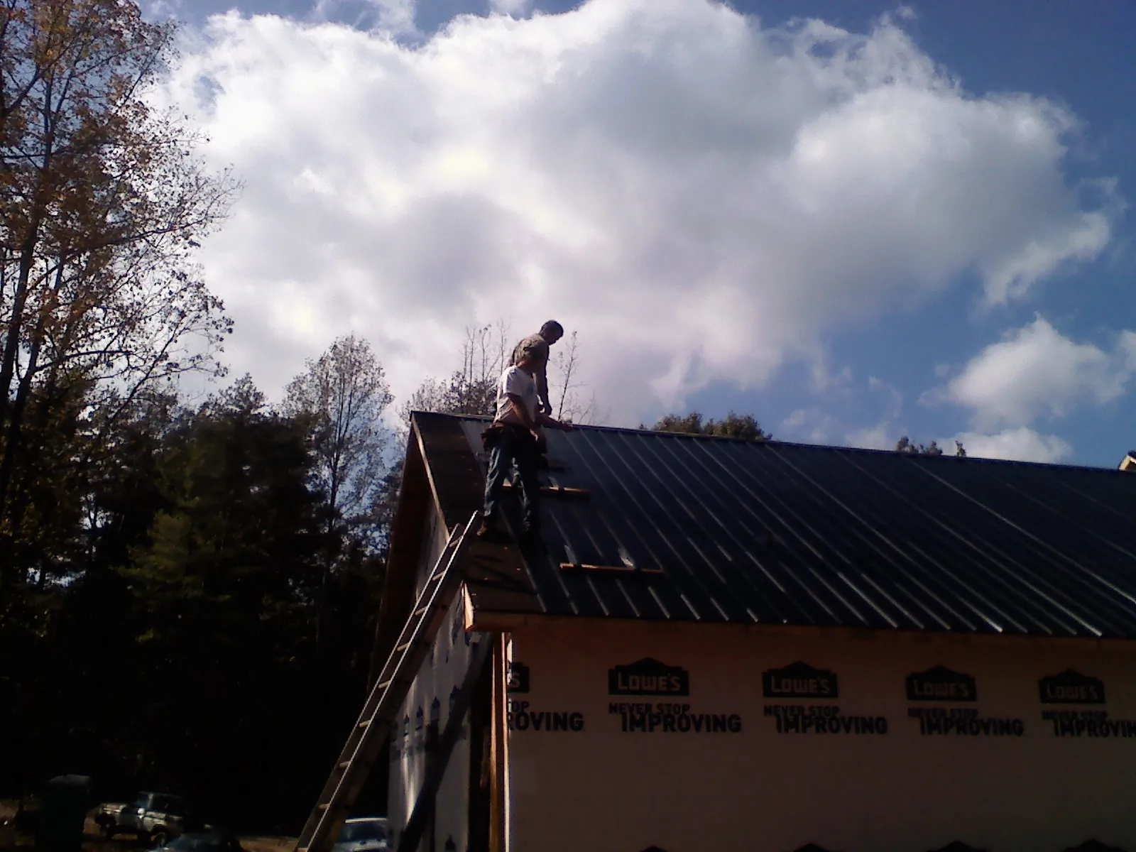 Roofer fastening dark metal panels high against a cloudy sky, from a Roof Inspection job in Woodacre